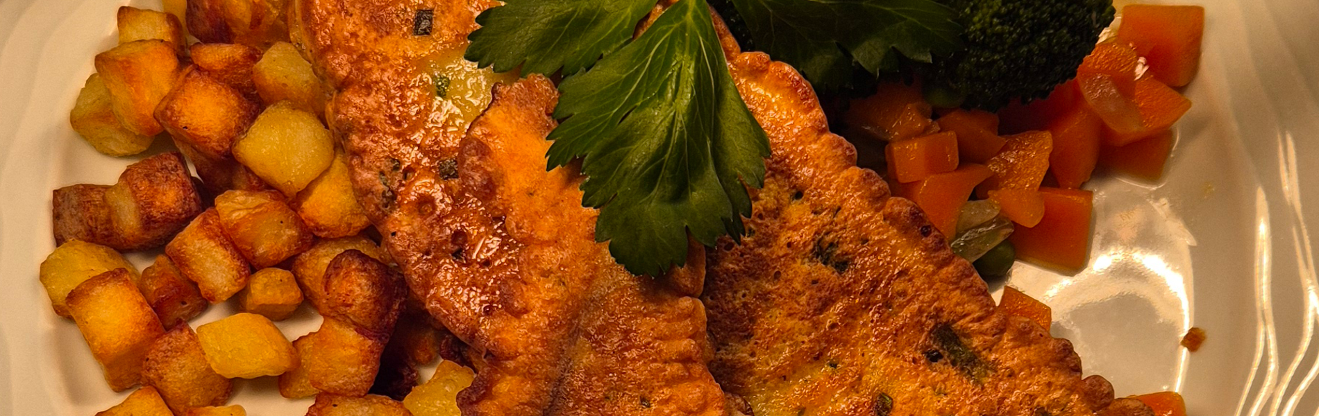 Buntbarschfilet in der Kräutereihülle auf frischem Gemüse und Würfelkartoffeln